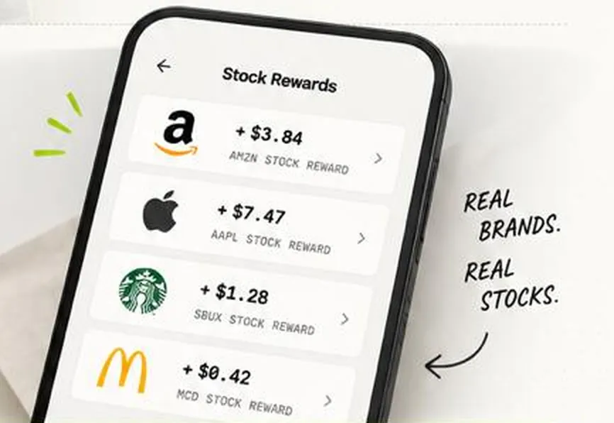 A phone showing stock rewards: +$3.84 AMZN, +$7.47 AAPL, +$1.28 SBUX, +$0.42 MCD